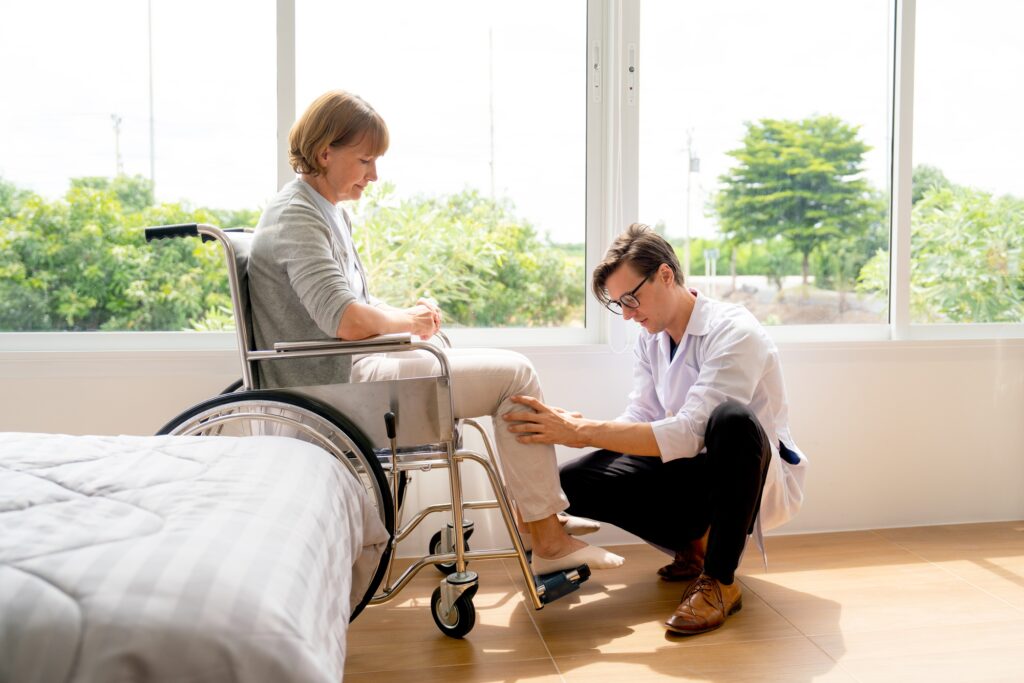 Young doctor sit and check problem and injury of leg and knee of senior woman who sit on wheelchair